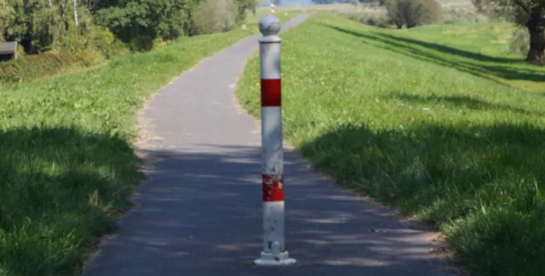 A red and white post stands in the middle of a narrow path that runs along the crown of an embankment.